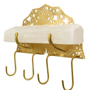 Op de afbeelding: Gouden metalen sleutelhanger met een wit rek en een stervormig ontwerp. De hanger heeft vier haken.