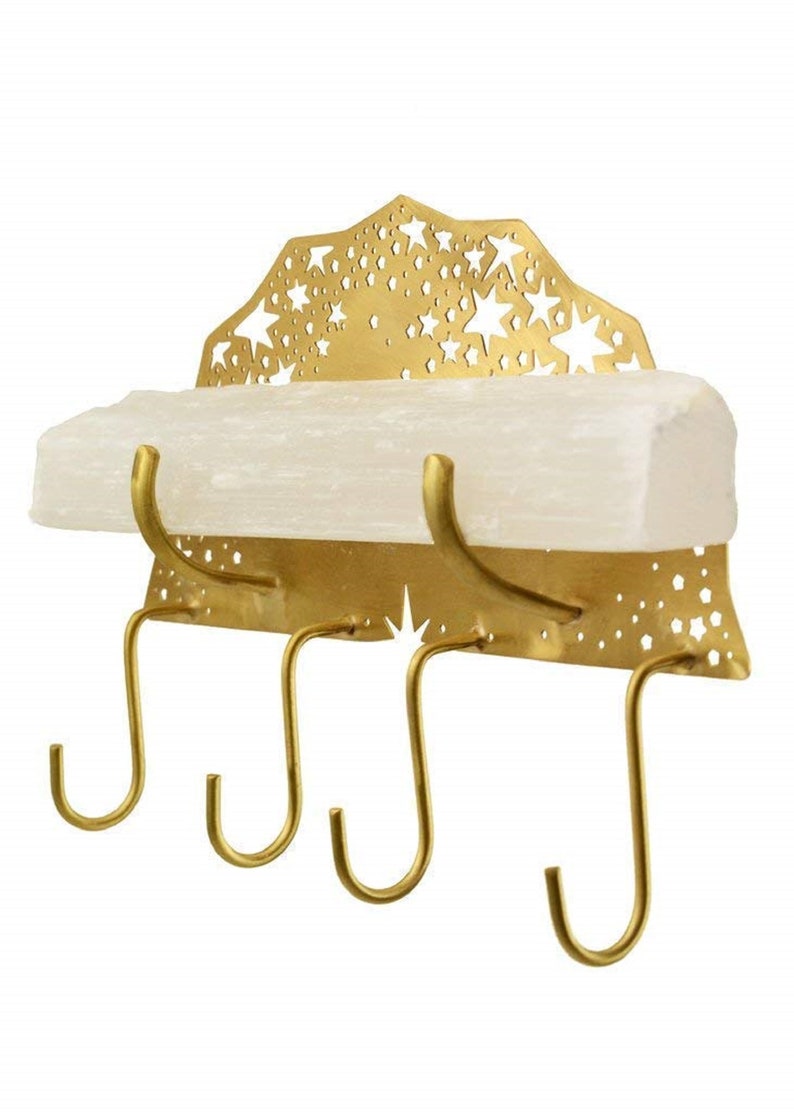 Op de afbeelding: Gouden metalen sleutelhanger met een wit rek en een stervormig ontwerp. De hanger heeft vier haken.