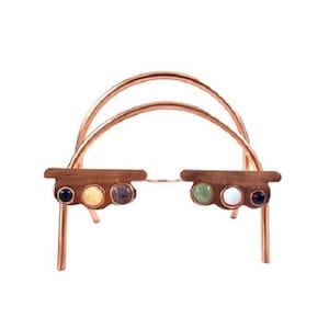 May include: A copper wire stand with a rounded arch shape. The stand has five gemstones embedded in the top, including a blue, yellow, gray, green, and white stone.