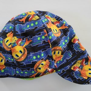 Pode incluir: Um gorro de solda de tecido preto, azul, verde, laranja e amarelo com um padrão repetido de personagens de desenhos animados e designs de placas de circuito.