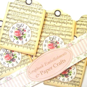 May include: A collection of rectangular paper tags featuring vintage sheet music backgrounds, floral clock illustrations, and metal eyelets. An oval label with the text Scrapbook Embellishments & Paper Crafts is placed over the tags.