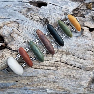 May include: A silver bracelet with seven oval-shaped stones in various colors, including white, red, green, black, and yellow. The stones are set in silver and connected by a silver chain.