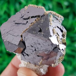 Puede incluir: Un grupo de cristales octa&eacute;dricos de color gris oscuro, met&aacute;licos, con un ligero brillo iridiscente. Los cristales est&aacute;n agrupados y tienen una superficie rugosa y texturizada.