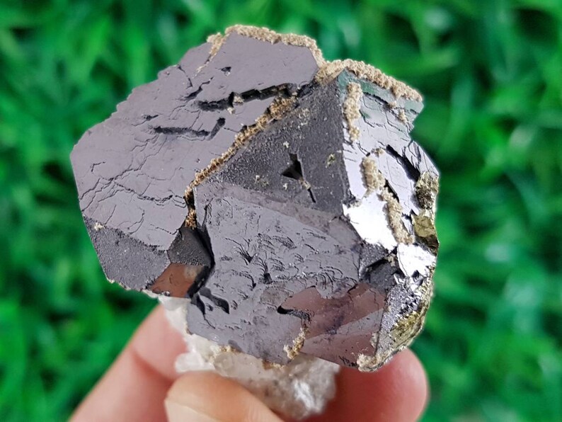 Puede incluir: Un grupo de cristales octa&eacute;dricos de color gris oscuro, met&aacute;licos, con un ligero brillo iridiscente. Los cristales est&aacute;n agrupados y tienen una superficie rugosa y texturizada.
