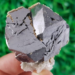 Puede incluir: Un cristal met&aacute;lico gris oscuro con forma geom&eacute;trica. El cristal tiene una superficie rugosa y texturizada y parece estar parcialmente roto.