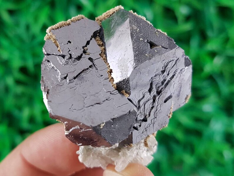 Puede incluir: Un cristal met&aacute;lico gris oscuro con forma geom&eacute;trica. El cristal tiene una superficie rugosa y texturizada y parece estar parcialmente roto.