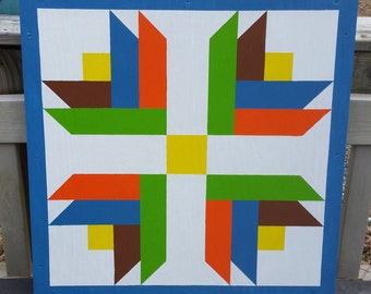 May include: A colorful quilt block with a geometric design. The block is made up of squares and triangles in shades of blue, green, orange, brown, and yellow. The block is framed with a blue border.