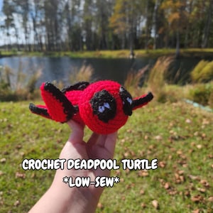 May include: Crocheted Deadpool turtle, red with black eyes and a black mouth, held in a hand. The text "CROCHET DEADPOOL TURTLE *LOW-SEW*" is below the turtle.