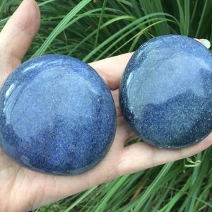 May include: Two smooth, polished, round stones with a deep blue color and subtle speckled texture. The stones have a glossy finish and are circular in shape, displaying a consistent dark blue hue across their entire visible surface area.
