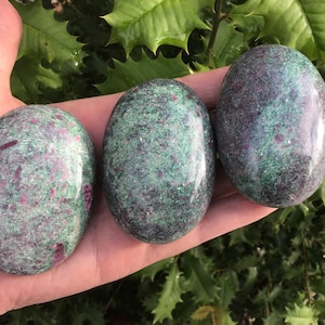 May include: Three polished oval stones featuring a mottled texture with deep green and vibrant magenta-red inclusions throughout. Each stone has a smooth, glossy surface that reflects light, showcasing the natural mineral patterns and color variations.