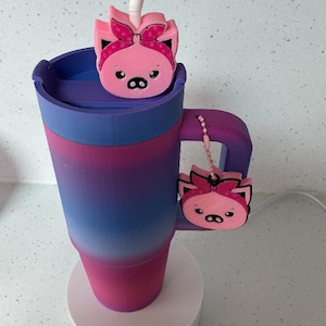 May include: A tall tumbler with a purple and pink gradient finish, featuring a matching purple lid and handle. Two pink pig-shaped charms with dark pink headbands are attached, one on the straw and one hanging from the handle by a small chain.