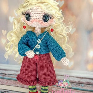 May include: A handmade crochet doll with long wavy blonde hair, large black eyes, and long eyelashes. The doll wears a teal button-up cardigan, maroon ruffled shorts, green and black striped socks, and red sneakers with white laces and red bead earrings.