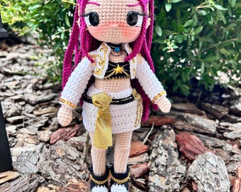 Puede incluir: Muñeca de ganchillo hecha a mano con tono de piel claro, cabello magenta y un atuendo blanco con detalles dorados. La muñeca lleva un top negro con una estrella dorada y una falda blanca con una faja dorada. Los zapatos de la muñeca son negros y blancos.