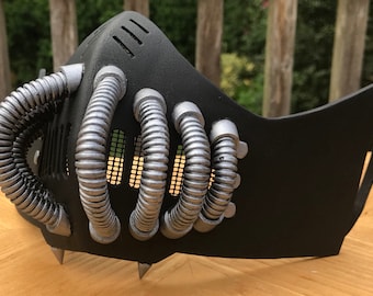 May include: A black and silver mask with a series of tubes and a mesh grill. The mask has a pointed chin and a strap on the back.