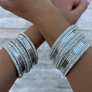 May include: A set of silver bangles with sparkling rhinestones. The bangles are stacked on each other and are worn on both wrists.