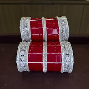 Può includere: Due pile di braccialetti rossi con abbellimenti color argento. I braccialetti hanno una finitura lucida e sono adornati con dettagli intricati. Gli accenti argentati aggiungono un tocco di eleganza al design tradizionale.