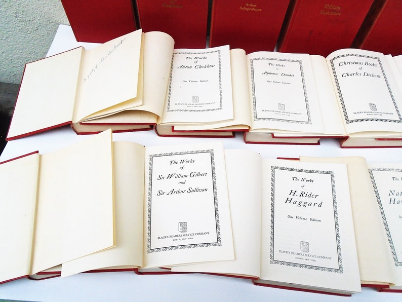 Pu&ograve; includere: Una collezione di libri in brossura rossa con scritte dorate sui dorsi. I libri sono disposti in una pila, con i titoli visibili. I titoli includono "Le Opere di Anton Čechov", "Le Opere di Alphonse Daudet", "Racconti di Natale di Charles Dickens", "Le Opere di Sir William Gilbert e Sir Arthur Sullivan", "Le Opere di H. Rider Haggard", e "Le Opere di Nathaniel Hawthorne".
