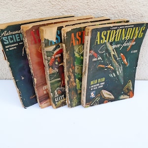 May include: A stack of vintage science fiction magazines with worn covers. The titles include "Astounding Science Fiction" and "Astounding Science-fiction". The covers feature colorful illustrations of spaceships and futuristic scenes. The magazines are from the 1940s.