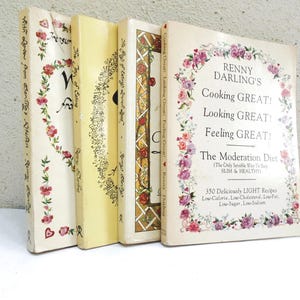 May include: A stack of vintage cookbooks with floral and decorative designs. The books have titles like "Renny Darling's Cooking Great!" and "The Joy of Eating." The covers feature pink and red roses.