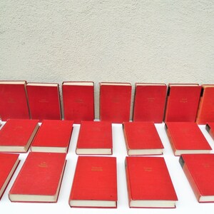 Pu&ograve; includere: Una collezione di ventiquattro libri in brossura rigida rossa con scritte dorate sui dorsi. I libri sono disposti in tre file di otto.