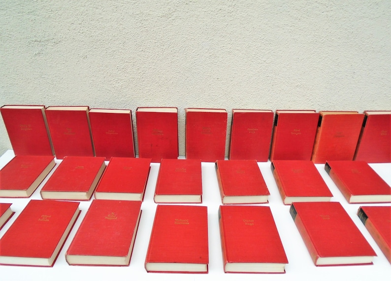 Pu&ograve; includere: Una collezione di ventiquattro libri in brossura rigida rossa con scritte dorate sui dorsi. I libri sono disposti in tre file di otto.