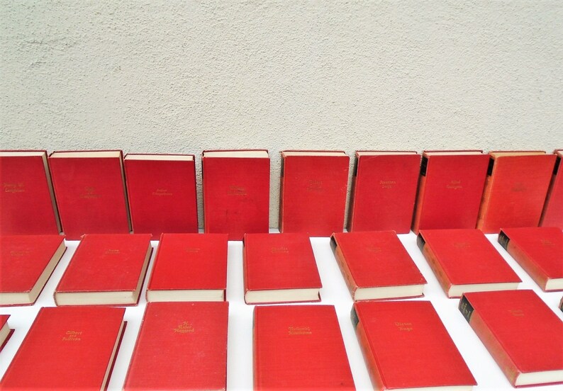 Pu&ograve; includere: Una collezione di 24 libri in brossura rigida rossa con scritte dorate sui dorsi. I libri sono disposti in tre file di otto libri ciascuna.