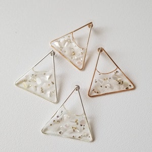 May include: Three pairs of triangle-shaped earrings with gold and silver wire frames. Each earring has a clear resin filling with embedded white and gold glitter.