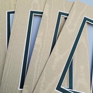 May include: A set of four rectangular paper photo mats featuring a textured beige surface with a wood grain pattern. Each mat has a dark forest green inner border and a thin white accent line surrounding the central rectangular cutout opening.