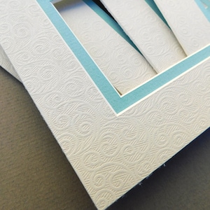 May include: Close-up of a white mat with a blue border. The mat has a textured surface with a repeating pattern of swirls.