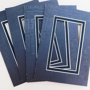Puede incluir: Cuatro passe-partout azul oscuro con bordes blancos y negros. Los passe-partout tienen una superficie texturizada y están diseñados para ser utilizados para enmarcar fotos u obras de arte.