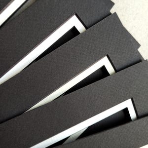 May include: A stack of black mat boards with white window openings. The mat boards are layered on top of each other, creating a visual pattern.