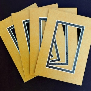May include: Four brown mat boards with black and white double mat openings. The mat boards are stacked on top of each other.