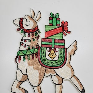 May include: Embroidered Christmas ornament featuring a brown llama carrying a stack of green and red wrapped gifts with a gold bell. The llama is wearing a red and green scarf and a green and white patterned saddle.