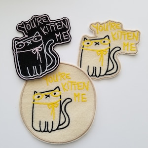May include: Three cat-themed patches with the phrase "You're Kitten Me". One patch is black with a white outline, another is white with yellow glasses, and the third is a beige circle with a cat design.