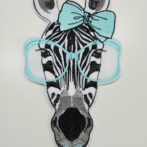 May include: Embroidered iron-on patch of a zebra wearing blue glasses and a blue bow. The zebra has black and white stripes.