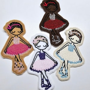 May include: Four embroidered felt patches of ballerinas in different poses. The ballerinas are wearing pink, red, blue, and white tutus. Each ballerina has a different hair color and skin tone.