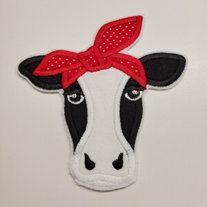Op de afbeelding: Een wit koeienhoofd met zwarte markeringen en een rode bandana met witte stippen die om het hoofd is gebonden.