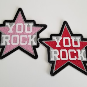 May include: Two embroidered iron-on patches in the shape of a star with the text "YOU ROCK" in white letters. One patch is pink with a gray outline and the other is red with a gray outline.