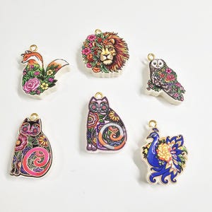 May include: Six flat, shaped pendants featuring colorful illustrations of a fox, a lion, an owl, two cats, and a peacock. Each animal is decorated with intricate floral patterns in various colors. Each pendant has a small gold-toned metal loop.