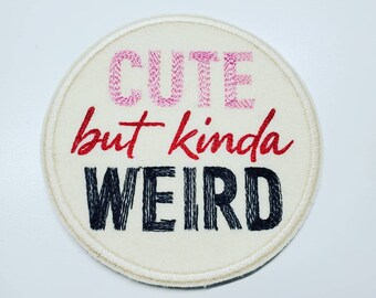 May include: A white round embroidered patch with the text "Cute but kinda weird" in pink, red, and black thread.