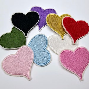 May include: Assortment of felt heart patches in various colors, including black, green, purple, gold, red, white, light blue, and pink. The hearts are all approximately the same size and shape.