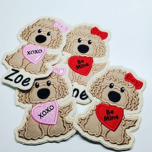 Puede incluir: Parches bordados con un perro de dibujos animados con pelo rizado, que lleva un lazo y un accesorio en forma de corazón. Algunos corazones dicen "XOXO" o "Be Mine". Un parche tiene el nombre "Zoe". Los parches son de color beige, rosa y rojo.