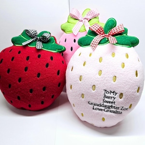 May include: Three plush strawberry pillows, one red, one pink, and one light pink. The pink pillow has gold embroidered dots and the text "To My Berry Sweet Granddaughter Zoe Love Grandma".