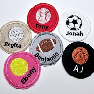 May include: Six round felt patches with embroidered sports balls and names. The patches are red, white, beige, gray, pink, and black. The sports include baseball, soccer, volleyball, football, tennis, and basketball.