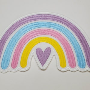 May include: A rainbow-colored embroidered patch with a purple heart in the center. The rainbow has five stripes: purple, blue, pink, yellow, and white.