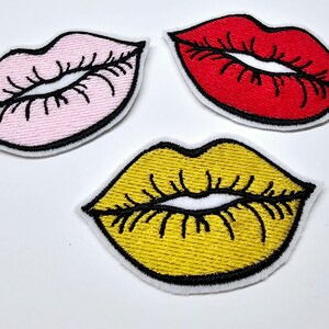 May include: Three embroidered lip patches in pink, red, and yellow. Each patch has a black outline and black stitched details for the lips. The patches are on a white background.