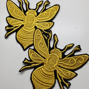 Pode incluir: Dois patches bordados de abelhas douradas com contornos pretos. As abelhas têm desenhos intrincados nas suas asas e corpos.