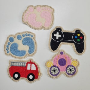 Könnte beinhalten: Gestickte Aufnäher mit einem rosa Babyfußabdruck, einem blauen Babyfußabdruck, einem roten Feuerwehrauto, einem schwarzen Videospiel-Controller und einer rosa Kutsche. Jeder Aufnäher hat einen beigen Rand und ist zum Aufnähen oder Aufbügeln auf Stoff bestimmt.