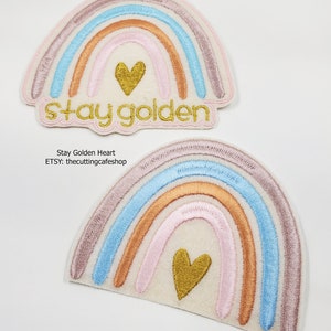 May include: Two embroidered iron-on patches featuring a rainbow with a gold heart in the center. The top patch has the text "Stay golden" in gold embroidery.