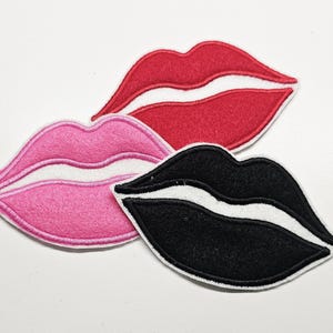 May include: Three embroidered lip patches in red, pink, and black. Each patch features a white inner lip and a white border. The patches are arranged on a white surface.